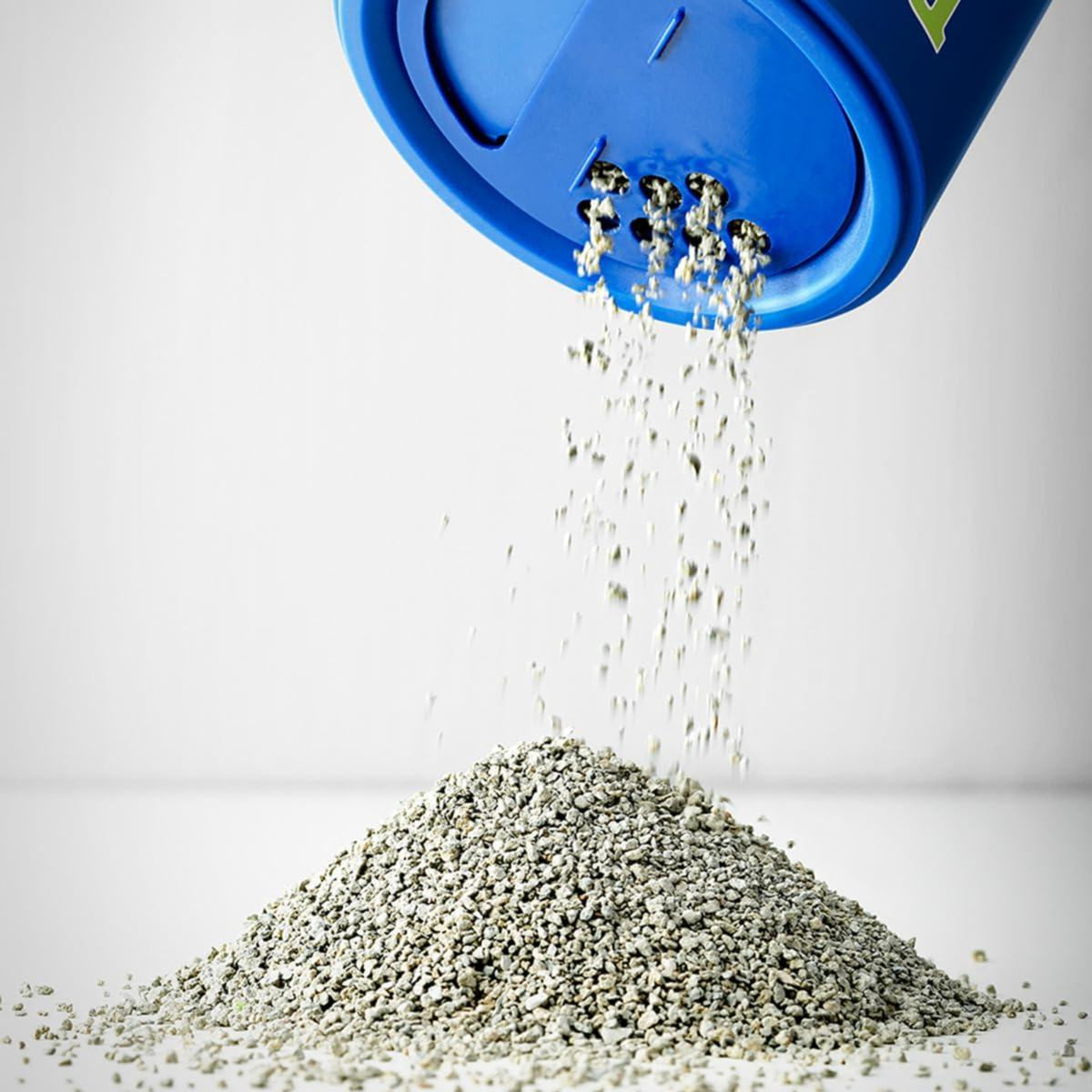 A blue container pouring a fine gray substance onto a mound.